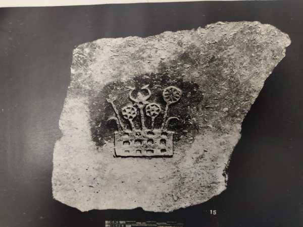 A shard from a ritual vessel adorned with sacred Buddhist symbols, including the Dharma and Triratna