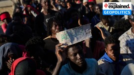 A migrant who crossed from Morocco into Spain holds a sign reading, "asylum" as he lines up for food distribution on a beach in Ceuta (AP Photo)