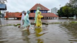 Children cover themselves as they move on a waterlogged road following rainfall in Kochi. (PTI Photo)