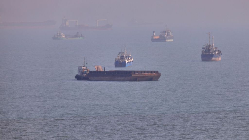 A small boat sails past cargo ships and other commercial vessels anchored in the Strait of Hormuz off Bandar Abbas, Iran