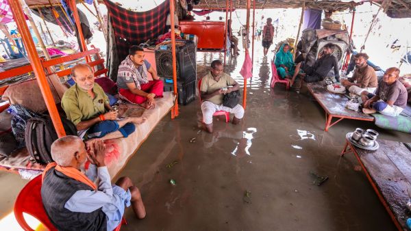 People sit in a waterlogged shelter along the banks of the swollen Ganges as the river's water level rises following heavy rainfall in Prayagraj. (PTI Photo)