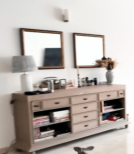 Floor-to-ceiling glass patio doors bring in natural light and are framed by rich teal curtains. The living space also features a wall-mounted television, low storage credenzas and indoor plants, giving the space a lived-in feel.