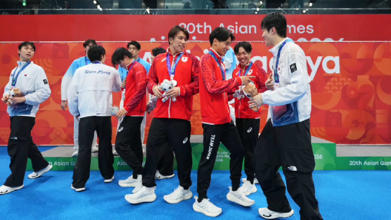 Gold medalist team China, rear in blue, silver medalist team Japan, in red, and bronze medalist team South Korea interact on the podium after the men's 4x200-meter freestyle relay final in swimming at the Asian Games in Tokyo, Japan, Monday, Sept. 21, 2026.