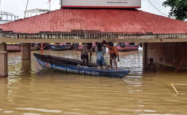 People duck on a wooden boat as they move on a partially submerged area after heavy rains, near Assi Ghat in Varanasi