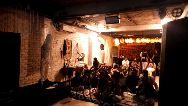 A crowd at an Out of Sequence gathering sits in the warmly lit venue while the movie starts 