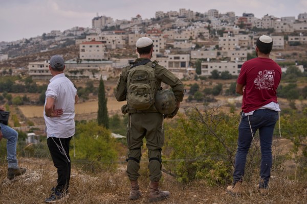 An Israeli soldier and settlers look out toward the Palestinian village of al‑Shuyukh from agricultural land near the Gad Natan settlement in the occupied West Bank.