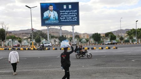 A vendor walks under a billboard showing Houthi leader Abdul Malik al-Houthi with a phrase that reads in Arabic: "The Saudi accusation against our people deserves to be described as the lie of the century" in Sanaa, Yemen (AP Photo)