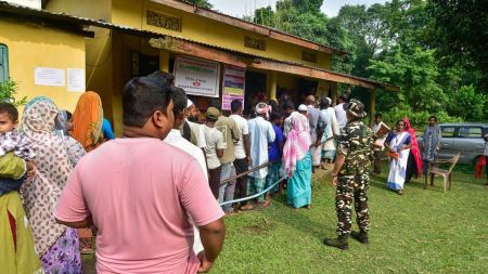 Morigaon, Oct 06 (ANI): Security personnel stand guard as voters queue to cast their vote for the Nagaon Lok Sabha by-election at Hatigarh, in Morigaon on Tuesday. (ANI Photo)